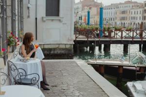 a woman sitting at a table by the water at Sina Palazzo Sant'Angelo in Venice