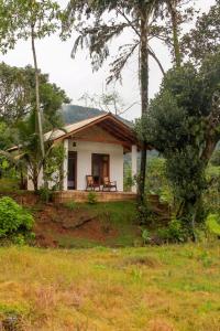 a small white house in the middle of a field at Forest & Fields Sinharaja in Deniyaya