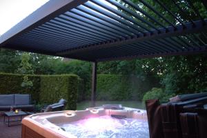 a patio with a hot tub under a black pergola at De Brittenburg 4-persoons, finse sauna, hottub, sunshower, grote zonnige omheinde tuin, wifi en huisdier vriendelijk in Lievelde