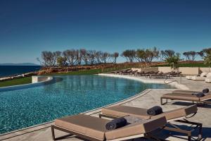 a swimming pool with lounge chairs and the ocean at Zelia Halkidiki, part of Destination by Hyatt - Adults Only in Nea Potidaea