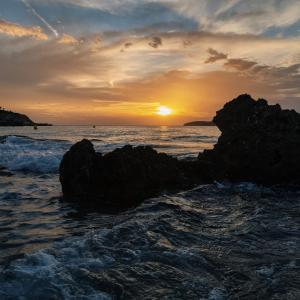 a sunset over the ocean with rocks in the water at Boutique Apartments Marsol Ibiza in Santa Eularia des Riu