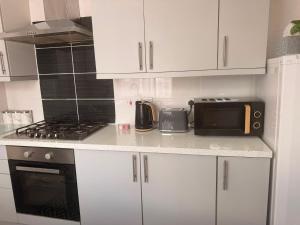 a kitchen with white cabinets and a stove and a microwave at Cosy Heavens in Quinton