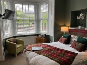 a bedroom with a bed and a chair and windows at Craigbank Guest House in Crianlarich