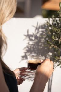 a woman holding a glass of coffee on a table at Mylopetra Suites Sarti in Sarti +15 photos