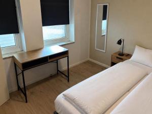 a bedroom with a bed and a desk and two windows at Klaksvik Mountain View Stay in Klaksvík