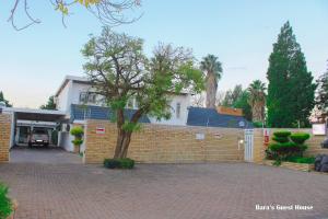 a brick fence with a tree in front of a house at Bara Guesthouse in Welkom