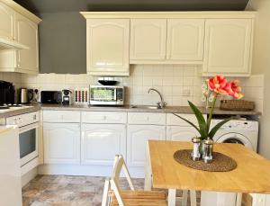 a kitchen with white cabinets and a wooden table with flowers at Stylish Countryside Loft near Silverstone-Bicester in Buckingham