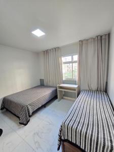 two beds in a room with a window at Praia Morro Katia apartamentos - Edificio Franklin Storck in Guarapari