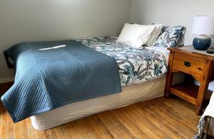 a bed with a blue comforter and a night stand at Papamoa Beach Sleepout in Papamoa