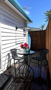 a patio table with two chairs and a vase with flowers at Papamoa Beach Sleepout in Papamoa