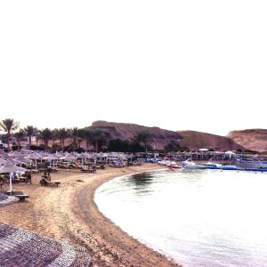 a beach with umbrellas and boats on the water at Xperience St. George Sharm El Sheikh in Sharm El Sheikh