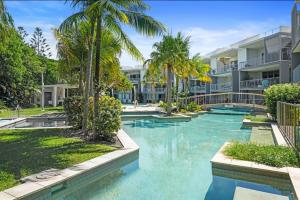a swimming pool with palm trees in front of a building at Drift North Beachfront Apartments - Private Apartments in Kingscliff