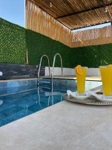 a pool with two glasses of orange juice on a table at Riad Jadis in Marrakesh