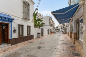 an empty street with white buildings and a blue awning at Casa Carpa Andalucia IV Carabeo Playa in Nerja