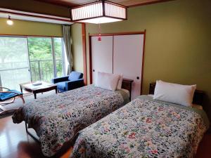 a bedroom with two beds and a chair and window at ウテナ2 in Ito