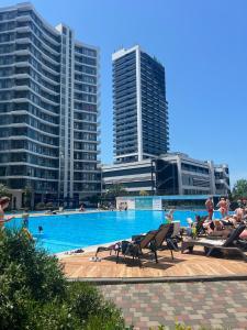 a swimming pool with people sitting in chairs and buildings at Квартира у моря с бассейном in Batumi