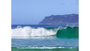 a wave in the ocean with a mountain in the background at Banyula Cove by Tiny Away in Barnes Bay