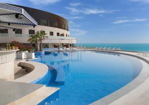 a large swimming pool next to a building with the ocean at Ray Hotel by Cloud 7 in Kuwait