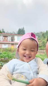 a baby is smiling while holding a spoon at Dhim in Mangpu
