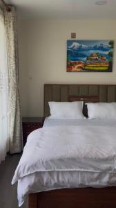 a bed with white sheets and a painting on the wall at Aranya Villa in Bākhri Kharka