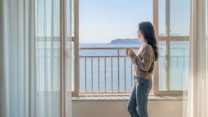 a woman standing on a balcony looking out at the ocean at Pohang Baritdol Pension in Pohang