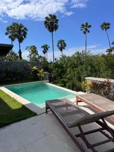 a swimming pool with a table and a bench and palm trees at Julim Flora - Eco Villa in Amed