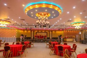 a banquet hall with red tables and chairs and a chandelier at Chitwan Grand Regency in Bharatpur