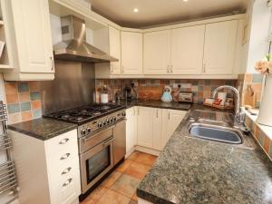 a kitchen with white cabinets and a stove and a sink at Rose Briar Cottage in Morpeth