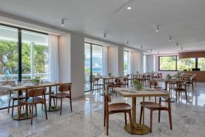 a dining room with tables and chairs and windows at Airotel Achaia Beach in Patra