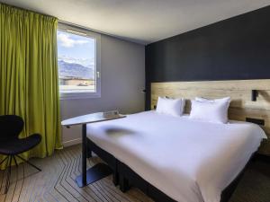 a bedroom with a large bed with a desk and a window at Ibis Styles Crolles Grenoble A41 in Crolles