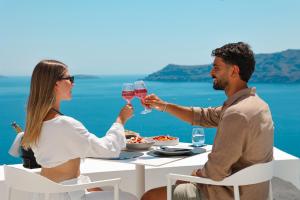 a man and woman sitting at a table with wine glasses at Saint Santorini in Oia