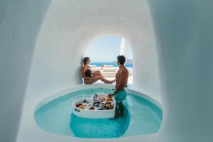 a man and a woman in a bath tub in a pool in a white house at Saint Santorini in Oia