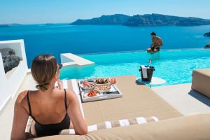 a woman sitting at a table with a tray of food next to a pool at Saint Santorini in Oia