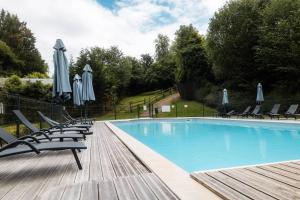 a swimming pool with chairs and umbrellas on a wooden deck at Domaine Guillaume Chalet 6p classic in Auquainville
