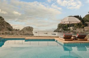 a swimming pool with two lounge chairs and an umbrella at Mazzarò Sea Palace - The Leading Hotels of the World in Taormina