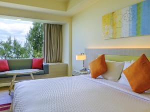 a bedroom with a bed and a couch and a window at Mercure Penang Beach in George Town