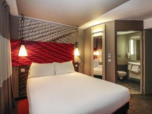 a bedroom with a large white bed and a bathroom at ibis Cahors in Cahors