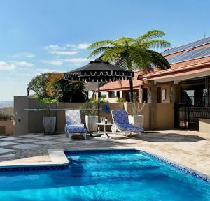 a swimming pool with two chairs and an umbrella at Big 5 Guest House Witbank in eMalahleni
