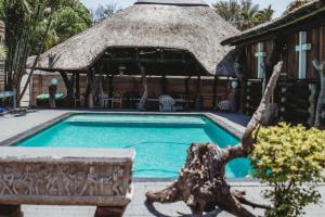 a swimming pool in front of a house with a thatch roof at Charming Self Catering Apartment in Phalaborwa