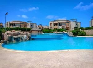 a large pool with blue water in front of houses at شالية ديمورا للعائلات in Dawwār Muḩammad Abū Shunaynah