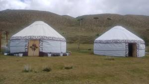 two large tents in a field with mountains in the background at Актан yurt cemp in Chong-Kyzylsu