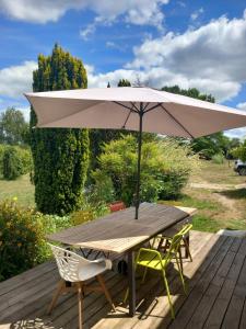 a wooden table with an umbrella on a deck at La yourte des Merveillaux in Riocaud