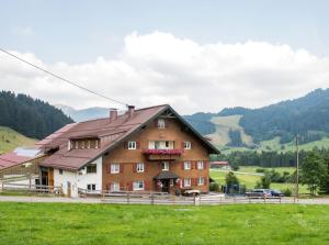 a large brown building in a field with mountains in the background at Bergbauernhof Haug in Bad Hindelang