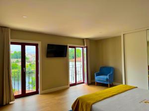 a bedroom with a bed and a blue chair and windows at Apartamentos Fonte Velha in Ponte da Barca