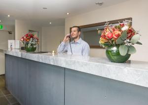 Ein Mann, der auf einem Telefon hinter einem Tresen mit Blumen redet in der Unterkunft Bankstown Motel 10 in Bankstown