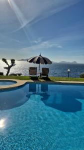 a swimming pool with an umbrella and chairs and the ocean at Ocean Breeze in Oya