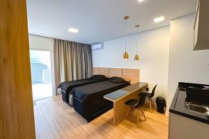 a bedroom with a bed and a desk and a kitchen at Condomínio Brises Downtown Garopaba in Garopaba +209 photos