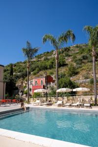 a swimming pool with chairs and palm trees and a mountain at Modica Inn Centro, BW Premier Collection in Modica