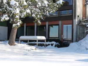 a snow covered bench next to a building with a tree at Alb-Refugium - beautiful, quiet in Schopfloch