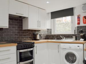 a kitchen with white cabinets and a washer and dryer at Cosy Cottage in Portinscale +8 photos